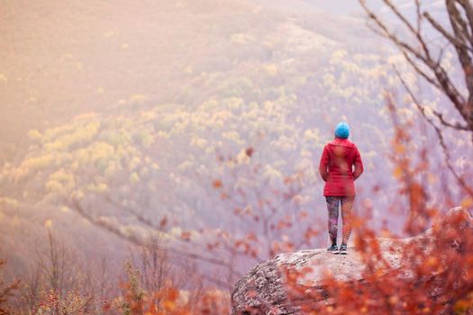 Hiking girl with poles and backpack standing on rocks. Windy autumn day. Travel and healthy lifestyle outdoors in fall season