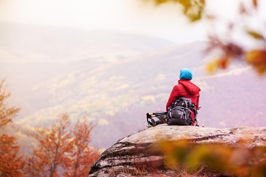 Hiker girl taking a rest on a rock in the mountains. Windy day. Travel and healthy lifestyle outdoors in fall season