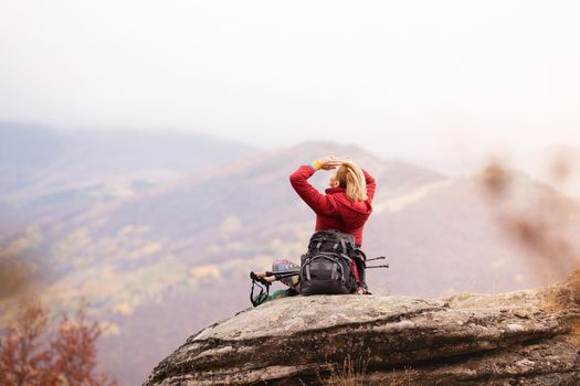 Hiker girl taking a rest on a rock in the mountains. Windy day. Travel and healthy lifestyle outdoors in fall season