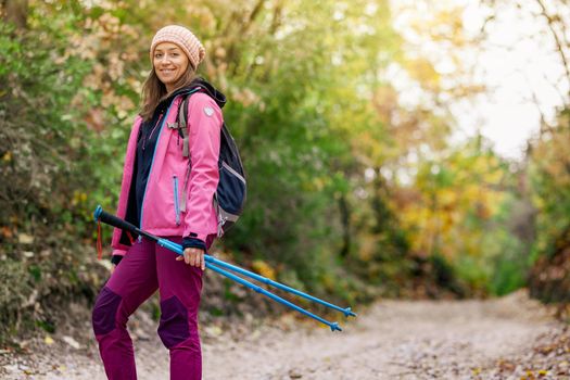 Hiker girl standing on a wide trail in the mountains. Backpacker with pink jacket in a forest. Healthy fitness lifestyle outdoors.