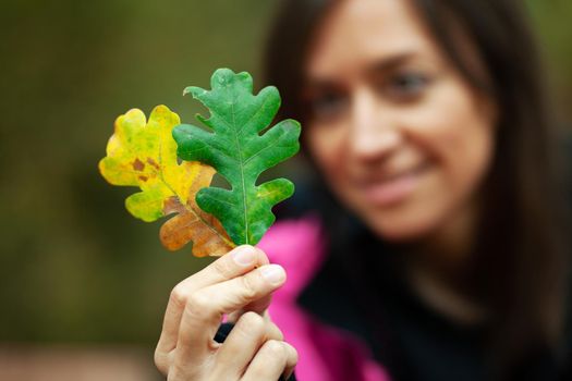 Girl in pink holding two autumn leaves. Fall season in the mountaing. Focus on leaves.