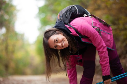 Hiker girl posing on a trail in the mountains. Backpacker with pink jacket in a forest. Healthy fitness lifestyle outdoors.