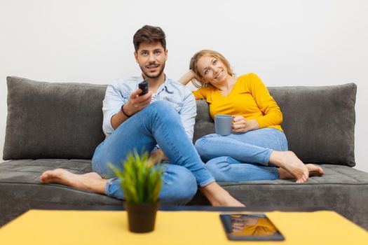 couple in love on a sofa watching tv, holding coffee and remote control