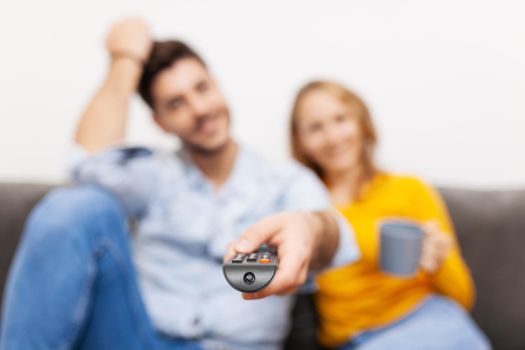 couple in love on a sofa watching tv, holding coffee and remote control