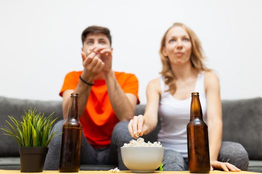 couple with beer bottles and popcorn watching sports game on tv. focus on bottles