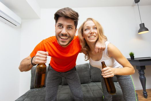 couple with beer bottles watching sports game on tv