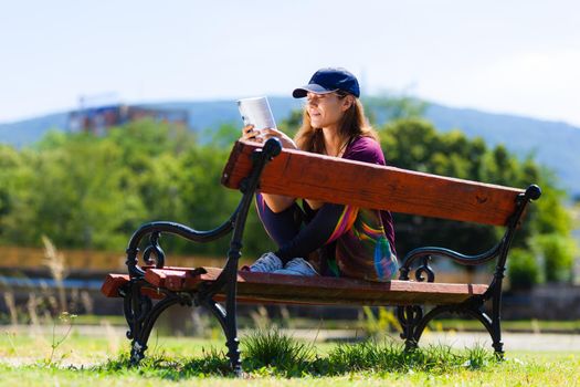 brunette girl with a cap, reading a book sitting on a bench