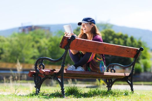 brunette girl with a cap, reading a book sitting on a bench