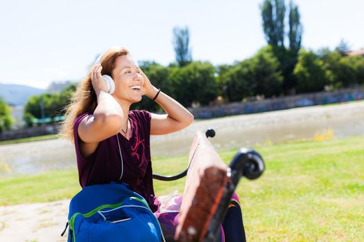 brunette girl with headphones and smartphone listening to music while sitting on a bench