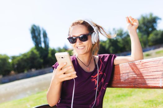 brunette girl with headphones, taking a selfie while sitting on a bench