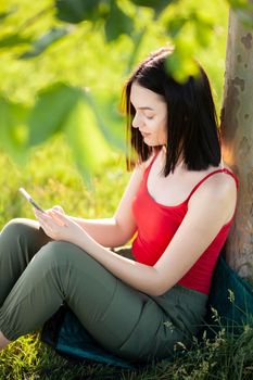 girl with dark brown hair using smartphone while sitting under a tree