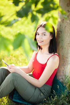 girl with dark brown hair using smartphone while sitting under a tree