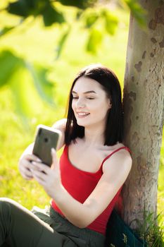 girl with dark brown hair using smartphone taking selfy under a tree