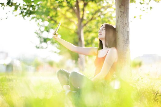 girl with dark brown hair using smartphone taking selfy under a tree