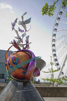 LIVERPOOL, ENGLAND, UK - JUNE 07, 2017: Peace on earth sculpture in honour of John Lennon with the Echo wheel of Liverpool to the rear at Keel Wharf, Liverpool, Merseyside, England, UK