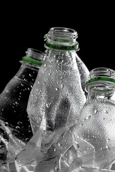 group of smashed empty plastic bottles with green caps, against black background