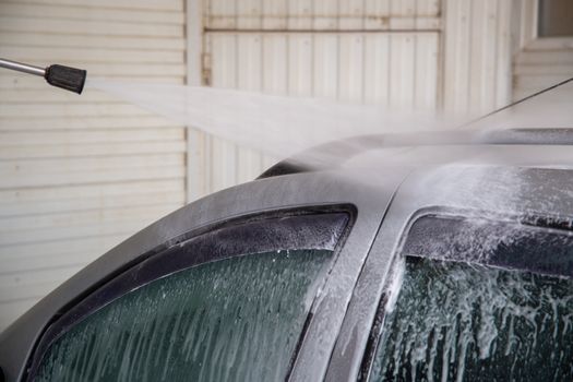 Indoor self service car wash process - close-up with selective focus and background blur. High pressure stream of water spraying on silver car's roof.