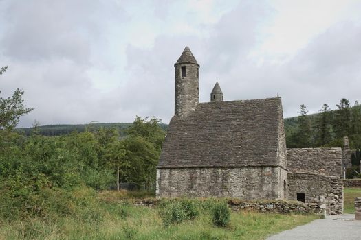 Glendalough, co. Wicklow, Ireland - August 10 2019 :Stone round tower and some ruins of a monastic settlement originally built in the 6th century in Glendalough valley, County Wicklow, Ireland.