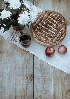 On the dining table on a glass tray is a delicious large homemade cake. On a napkin near tea in a glass and apples.