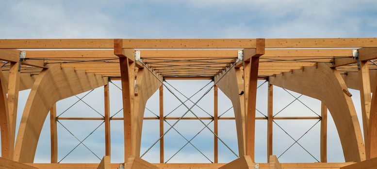 Detail of a modern wooden architecture in glued laminated timber on a blue cloudy sky