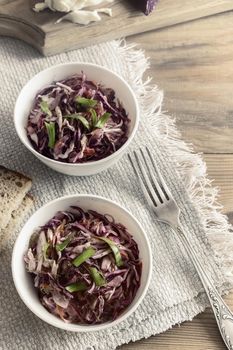 On a wooden table on a napkin, a salad of red and white cabbage with green onions. The concept of healthy eating. The view from the top.