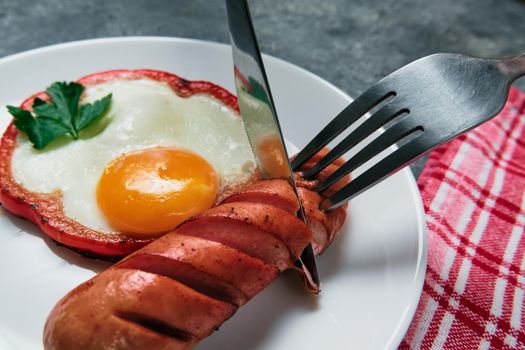 fried egg, red pepper, sausage, towel and cutlery on a dark table