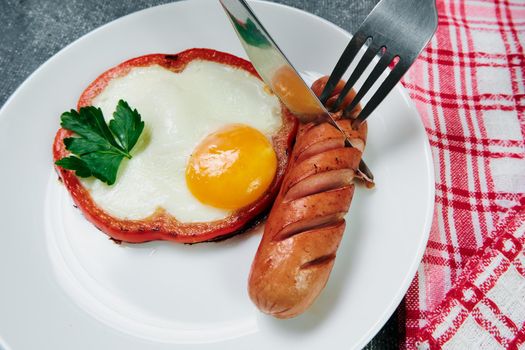 fried egg, red pepper, sausage, towel and cutlery on a dark table