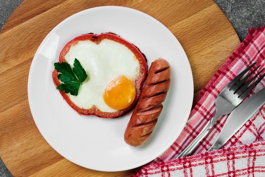 fried egg, red pepper, sausage, towel and cutlery on a dark table