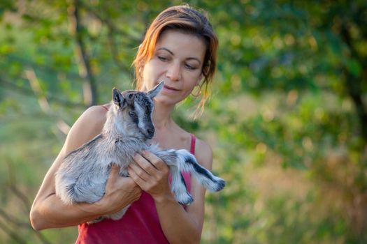 Beautiful woman with a small and nice goatling on her hands in a green background