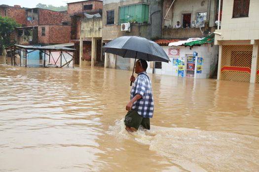 salvador, bahia / brazil - April 27, 2015: Young man is seen with surfboard in flooded area during rainy season community of Bate-faxo in the city of Salvador.