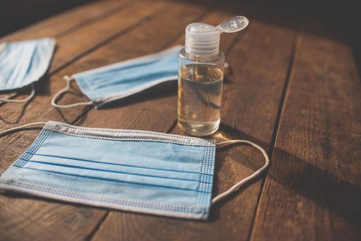 plastic bottle with hand sanitizer and disposable masks lie on a wooden table