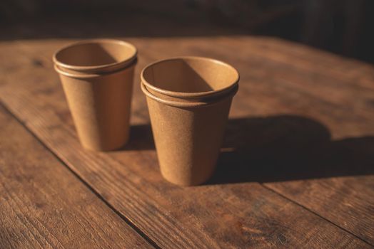 Disposable dark brown kraft paper cups stand on wooden table against brown background