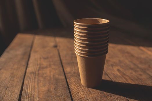 Disposable dark brown kraft paper cups stand on wooden table against brown background