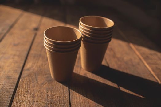 Disposable dark brown kraft paper cups stand on wooden table against brown background