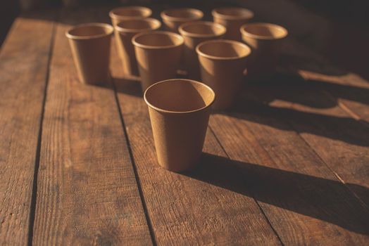 Disposable dark brown kraft paper cups stand on wooden table against brown background