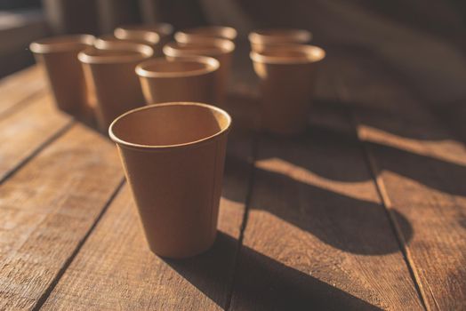 Disposable dark brown kraft paper cups stand on wooden table against brown background