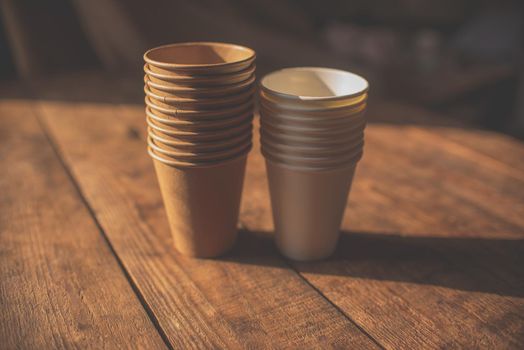 disposable cups made of dark brown paper and white cups stand on wooden table against brown background