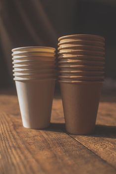 disposable cups made of dark brown paper and white cups stand on wooden table against brown background