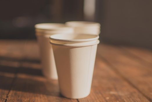 disposable white cardboard cups stand on a wooden table on a brown background