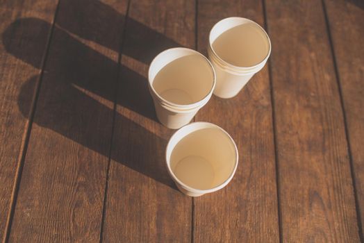 disposable white cardboard cups stand on a wooden table on a brown background