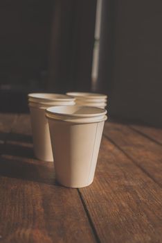 disposable white cardboard cups stand on a wooden table on a brown background