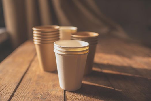 disposable cups made of dark brown paper and white cups stand on wooden table against brown background