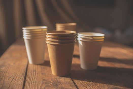 disposable cups made of dark brown paper and white cups stand on wooden table against brown background