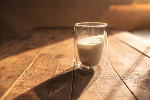 double glass with yogurt on a wooden table where the bright sun is shining