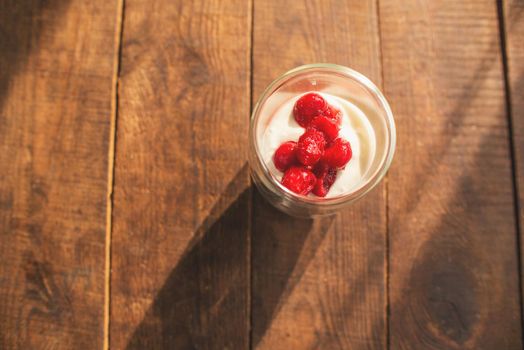 double glass with yogurt and berries on a wooden table where the bright sun is shining