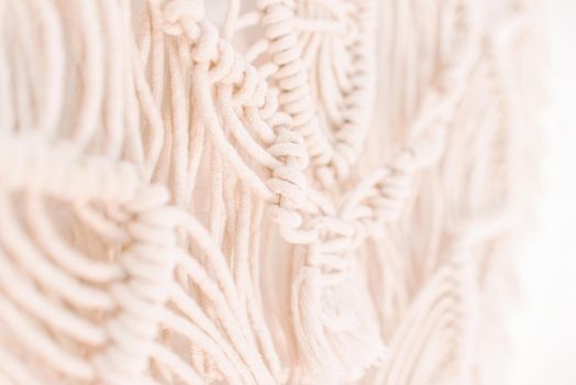 fragment of wall panel in boho style made of cotton threads of natural color using macrame technique for home and wedding decor.