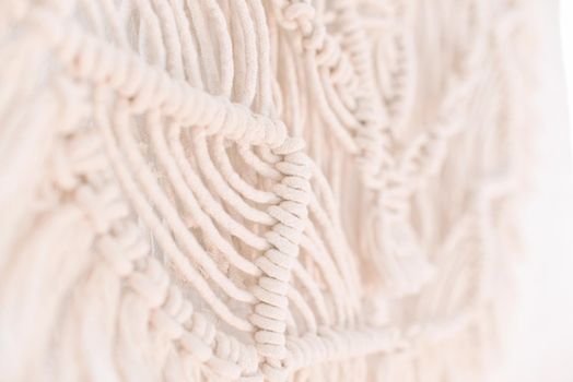 fragment of wall panel in boho style made of cotton threads of natural color using macrame technique for home and wedding decor.