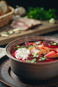 Freshly cooked borscht - traditional dish of Russian and Ukrainian cuisine in earthenware dishes with bacon, sour cream and garlic, vertical image.