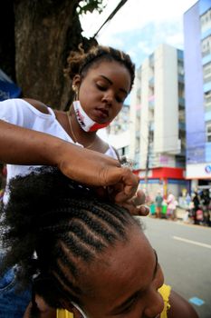 salvador, bahia, brazil - december 14, 2020: Young man is seen making afro moths on the hair of a black woman on the street in downtown Salvador.