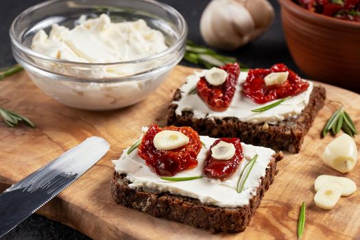 Homemade multigrain bread sandwiches with cream cheese and sun-dried tomatoes on a wooden platter, close-up. Healthy eating concept.